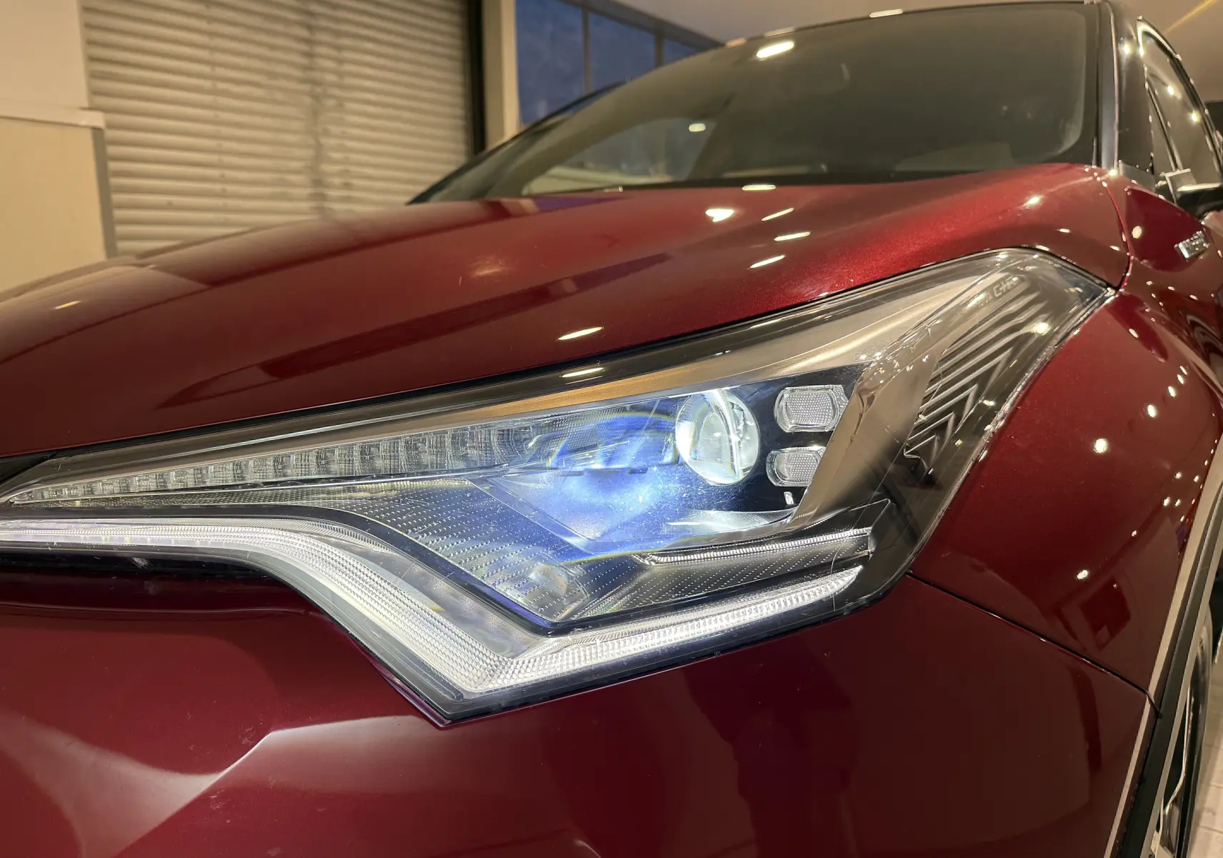 Gros plan sur le phare avant droit du Toyota C-HR Hybride rouge, mettant en valeur son design LED distinctif.