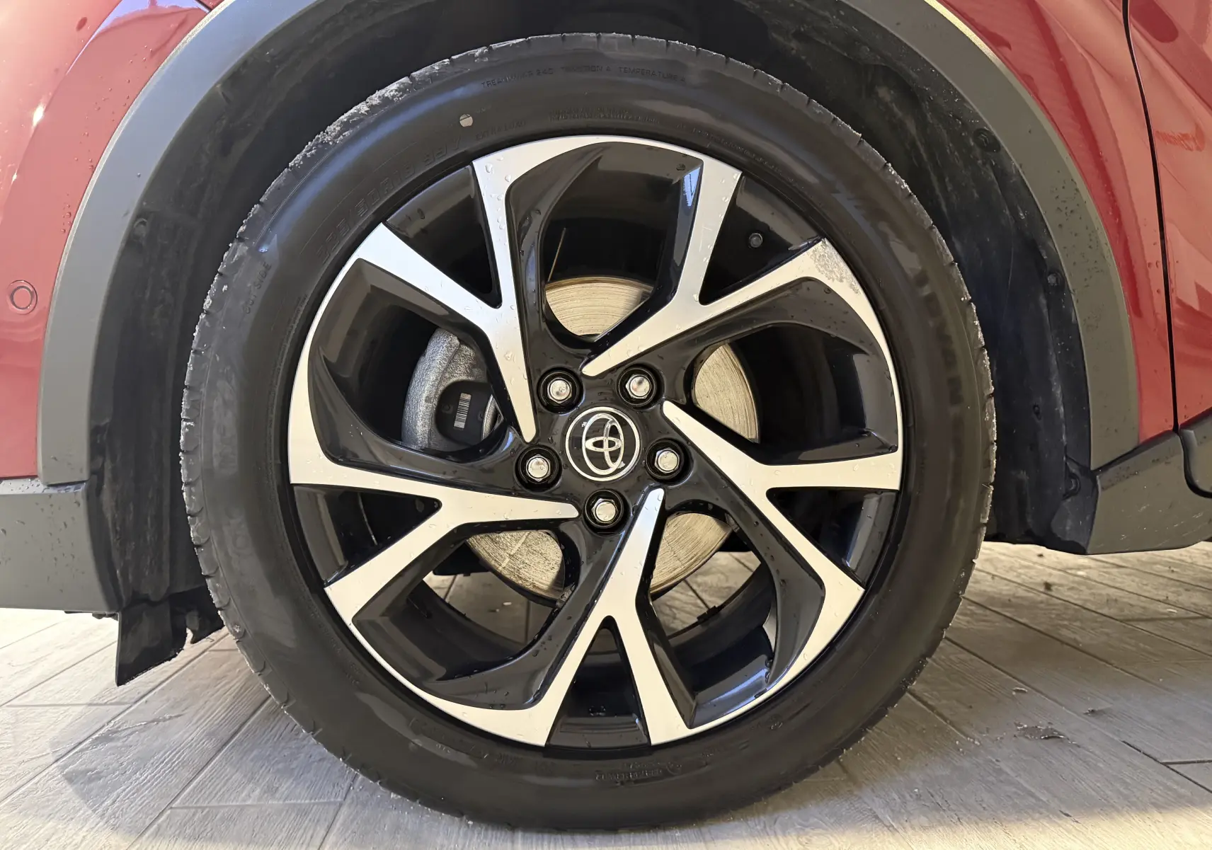 Gros plan sur la roue avant droite du Toyota C-HR Hybride rouge, mettant en valeur la jante alliage bicolore au design dynamique.