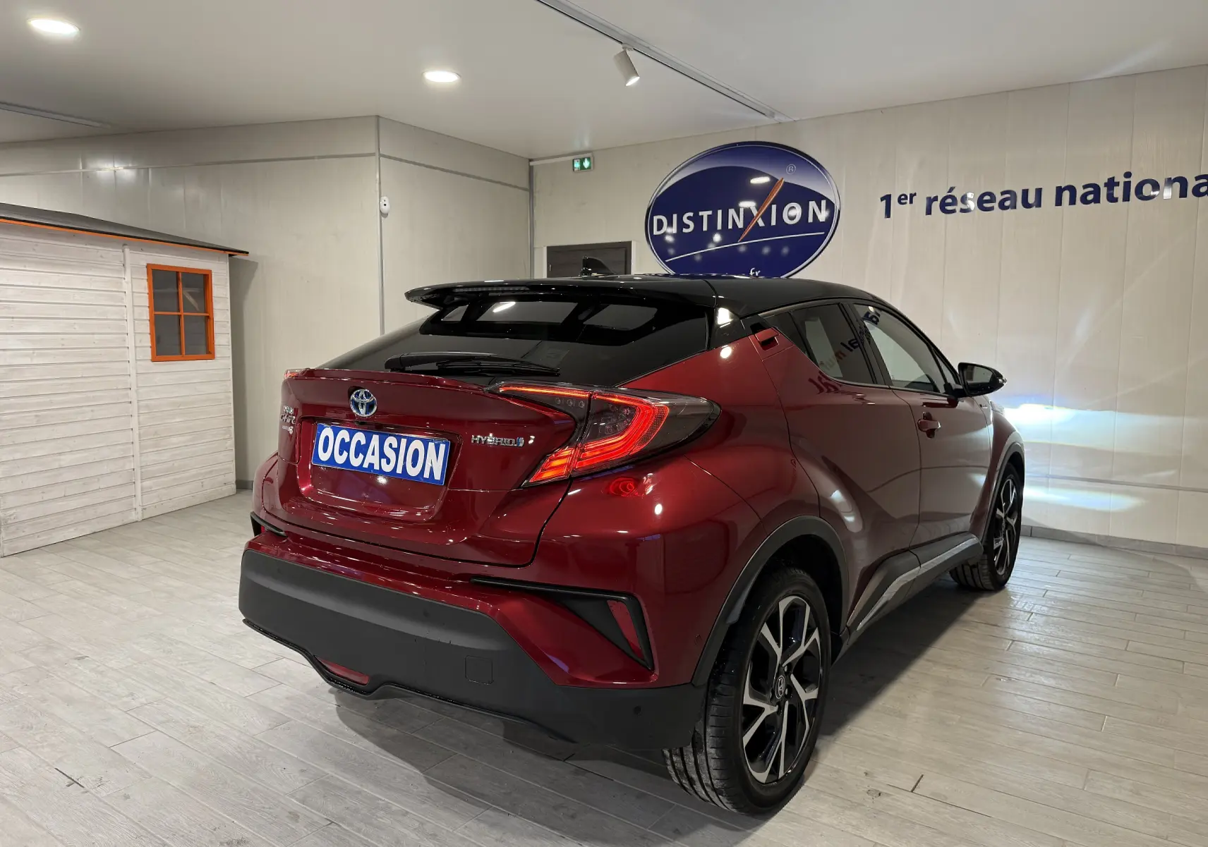 Vue 3/4 arrière droite d'un Toyota C-HR Hybride rouge avec toit noir et feux arrière LED distinctifs.