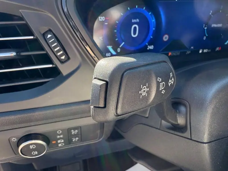 Gros plan sur la commande de clignotants et phares du Ford Kuga 2024, tableau de bord numérique bleu en arrière-plan.