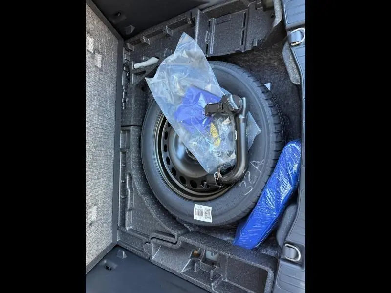 Vue du coffre du Ford Kuga 2024 montrant la roue de secours noire et les outils de changement emballés en plastique.