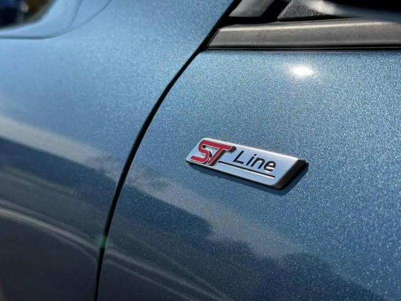 Gros plan sur l’écusson ST-Line rouge et noir sur la carrosserie bleu métallisé côté gauche du Ford Kuga 2024.