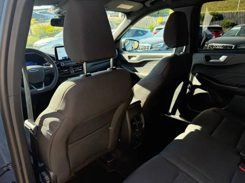 Vue intérieure arrière du Ford Kuga bleu 2024, sièges sport noirs avec surpiqûres rouges et tableau de bord visible.