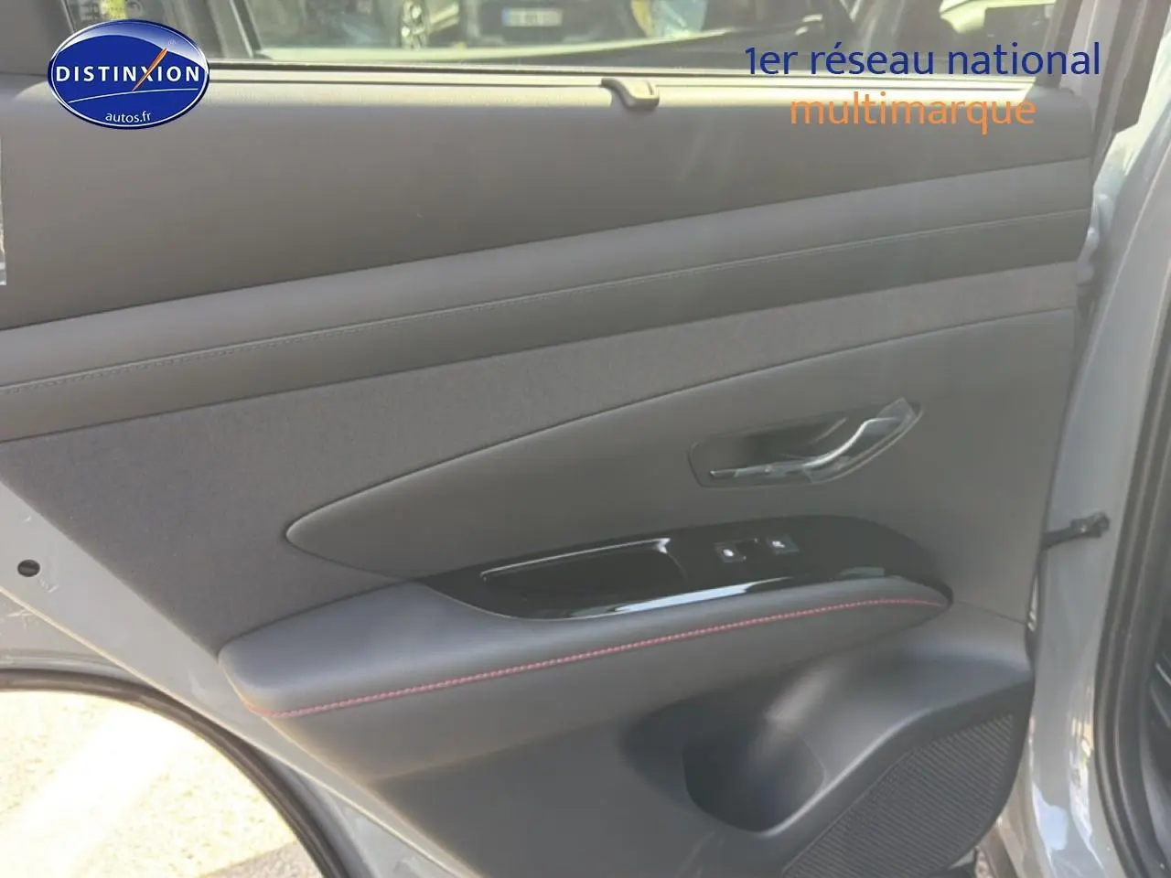 Vue intérieure côté gauche de la porte arrière gris shadow du Hyundai Tucson 2026 avec surpiqûres rouges et commandes vitres.
