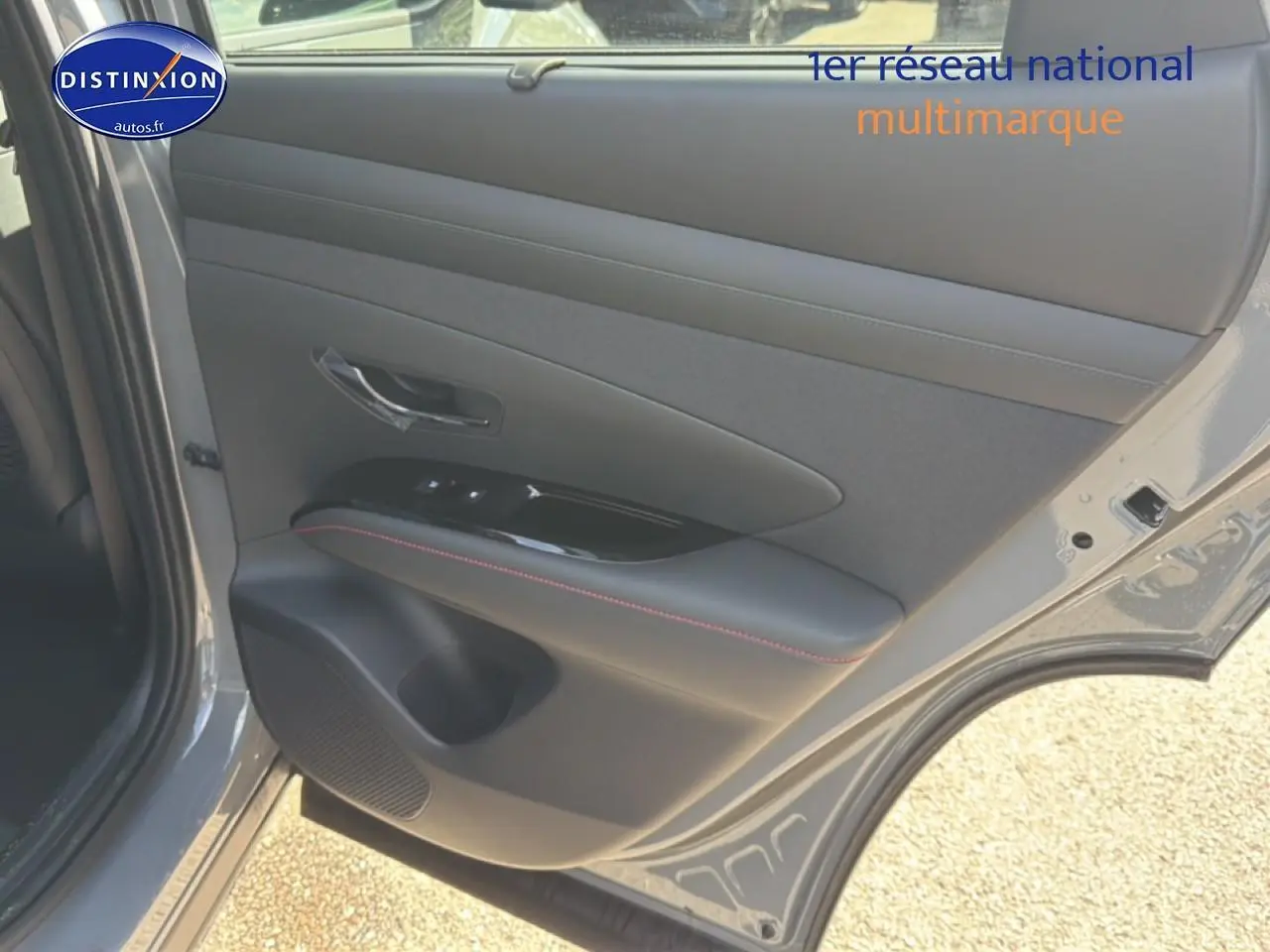Vue intérieure du panneau de porte arrière droite gris shadow du Hyundai Tucson 2026 avec surpiqûres rouges et commande de vitres.