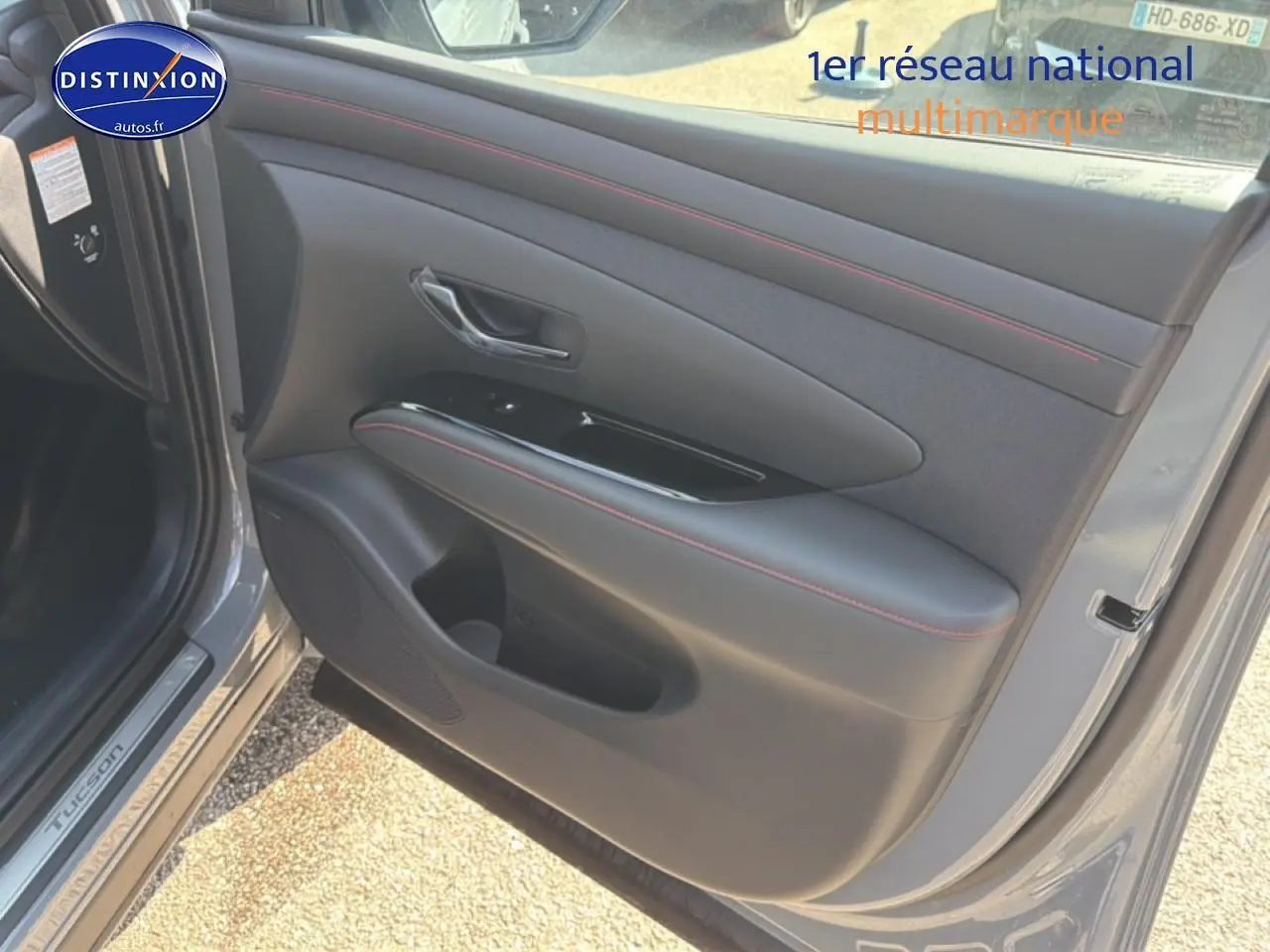 Vue rapprochée de la porte avant gauche gris shadow du Hyundai Tucson 2026 avec surpiqûres rouges et poignée chromée.