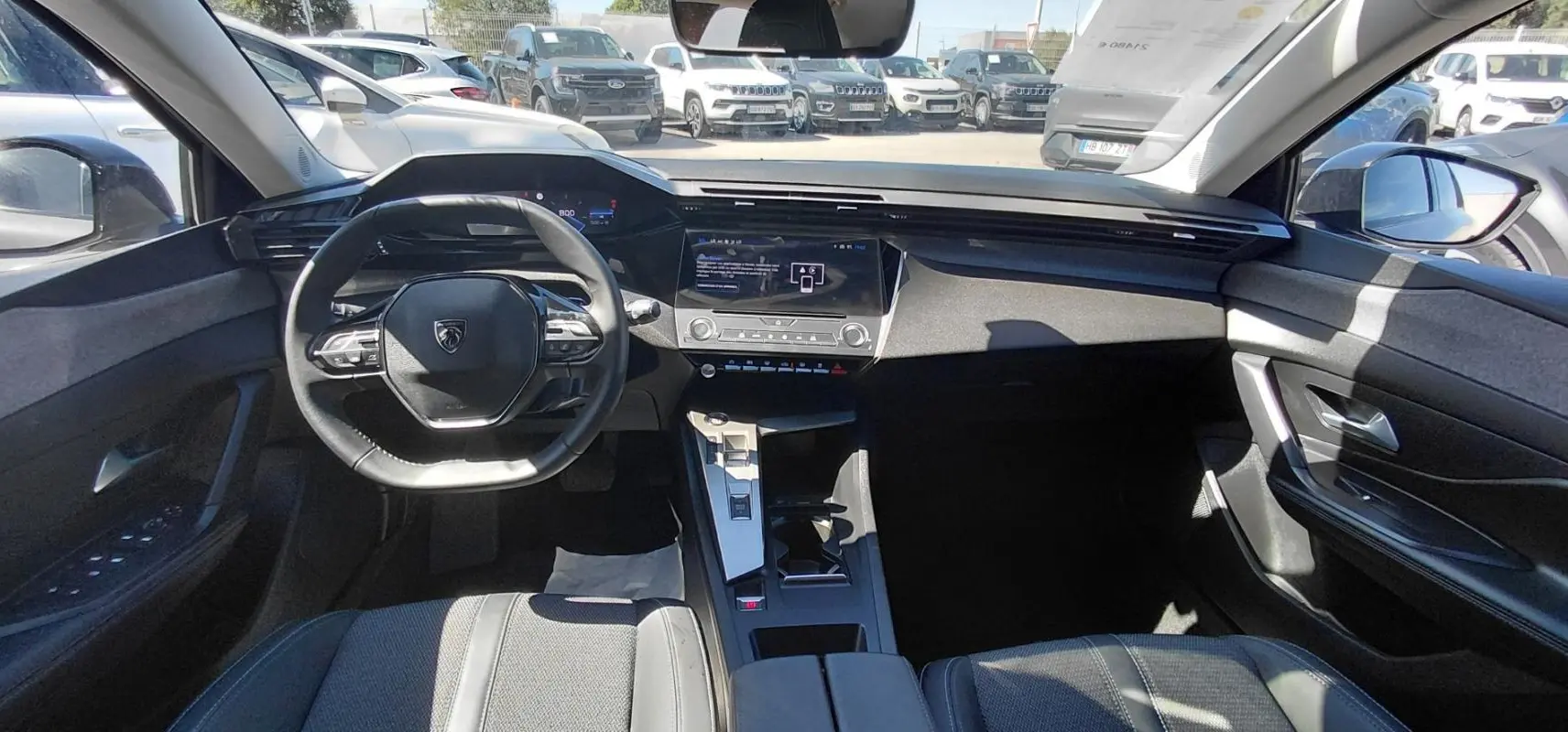 Vue intérieure avant du Peugeot 308 gris 2025, mettant en valeur le volant compact et le cockpit numérique moderne.