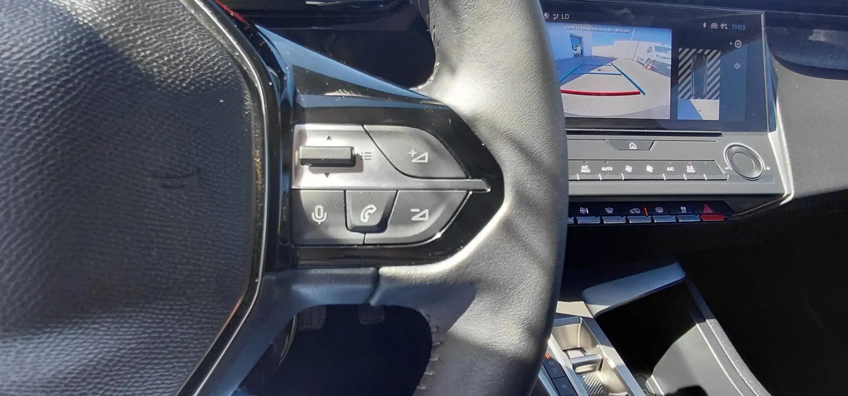 Gros plan sur le volant cuir noir et les commandes intégrées, avec l'écran tactile affichant la caméra de recul du Peugeot 308 gris.