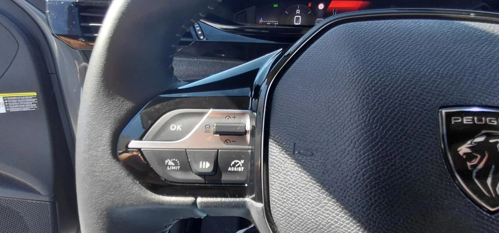 Gros plan sur le volant noir de la Peugeot 308 2025, montrant les commandes du régulateur et le logo lion au centre.