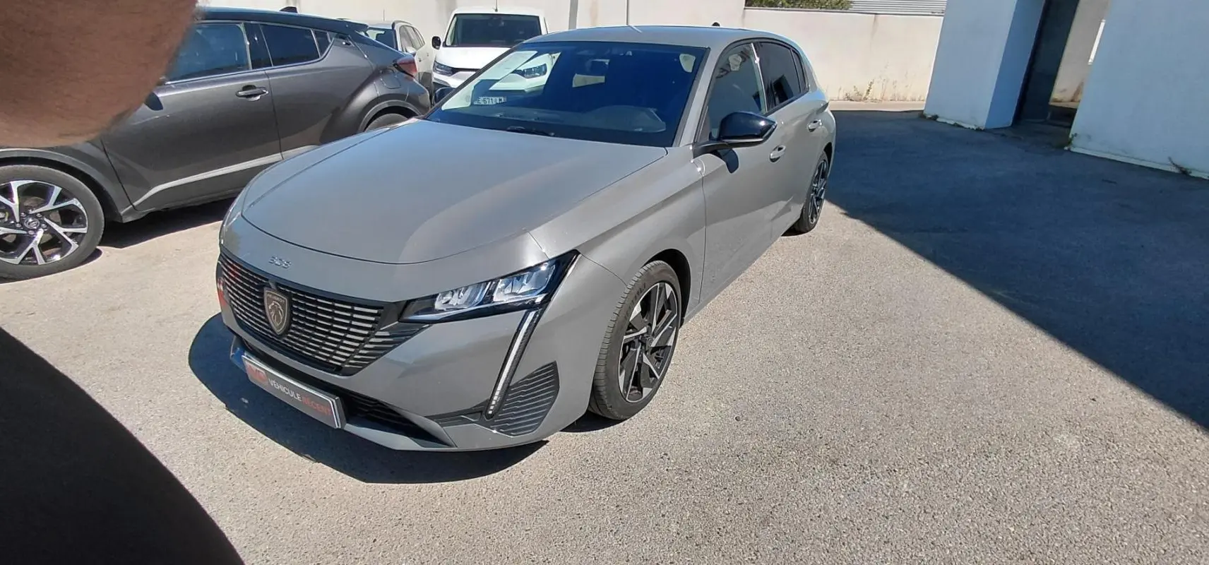 Peugeot 308 gris vue 3/4 avant droit, mettant en valeur sa calandre distinctive et ses phares LED fins.