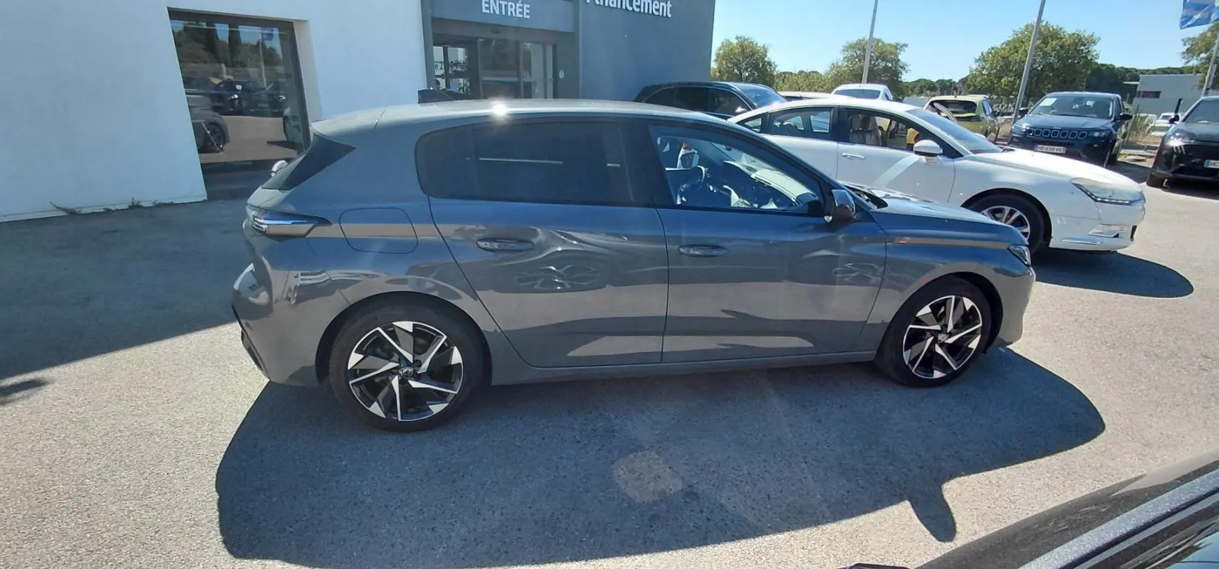 Vue de profil côté droit d'une Peugeot 308 gris métallisé garée en extérieur, avec jantes alliage distinctives.