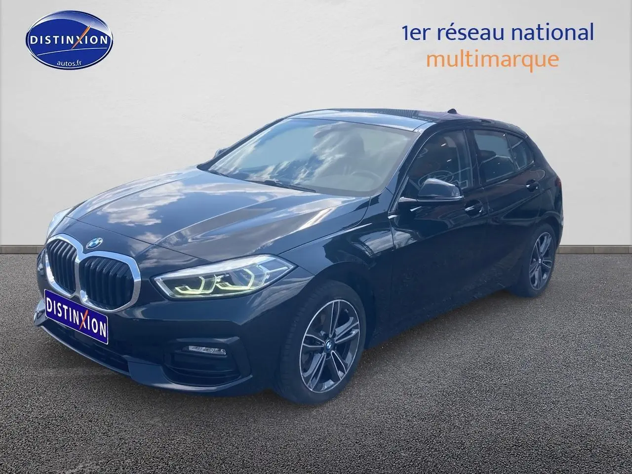 BMW Série 1 noire vue en 3/4 avant droit, avec phares LED allumés et jantes alliage double rayons.