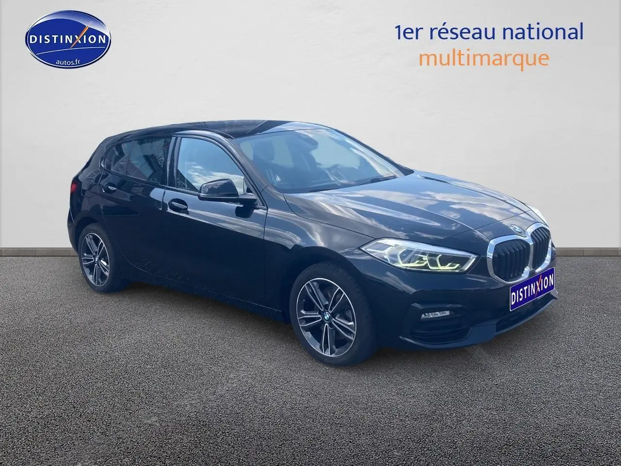 BMW Série 1 noire vue en 3/4 avant droit avec phares LED allumés et jantes alliage 17 pouces double rayons.