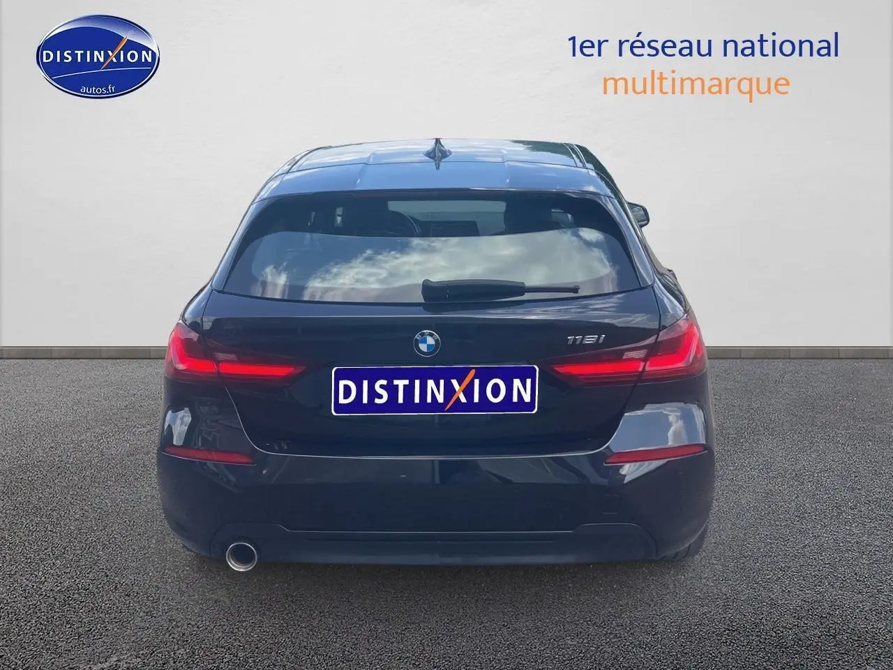 Vue arrière d'une BMW Série 1 noire (118i) avec feux LED allumés et logo distinctif sur fond clair.