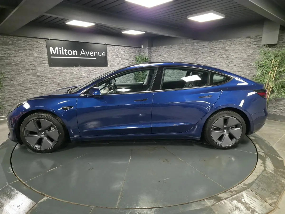 Profil côté gauche d'une Tesla Model 3 RWD 2021 bleu foncé avec jantes 18 pouces en aluminium dans un showroom.