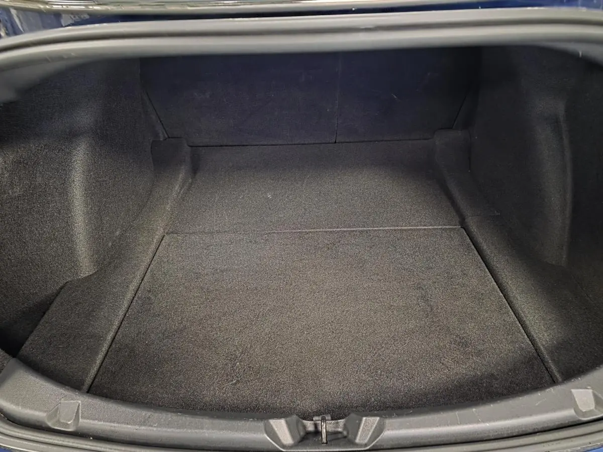 Coffre ouvert en vue plongeante d'une Tesla Model 3 RWD bleu foncé, montrant un espace de rangement vide et tapissé.