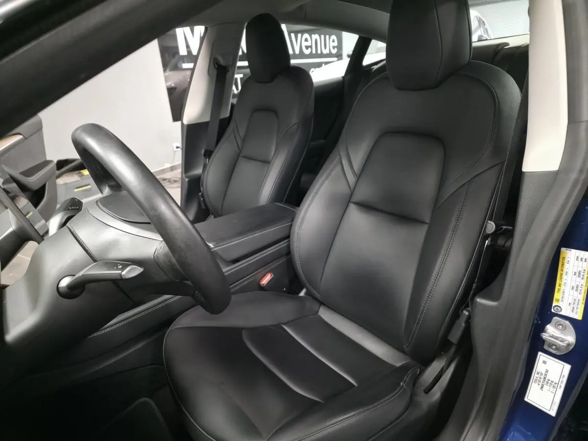 Intérieur noir de la Tesla Model 3 RWD 2021, vue côté conducteur avec sièges en cuir et accoudoir central visible.