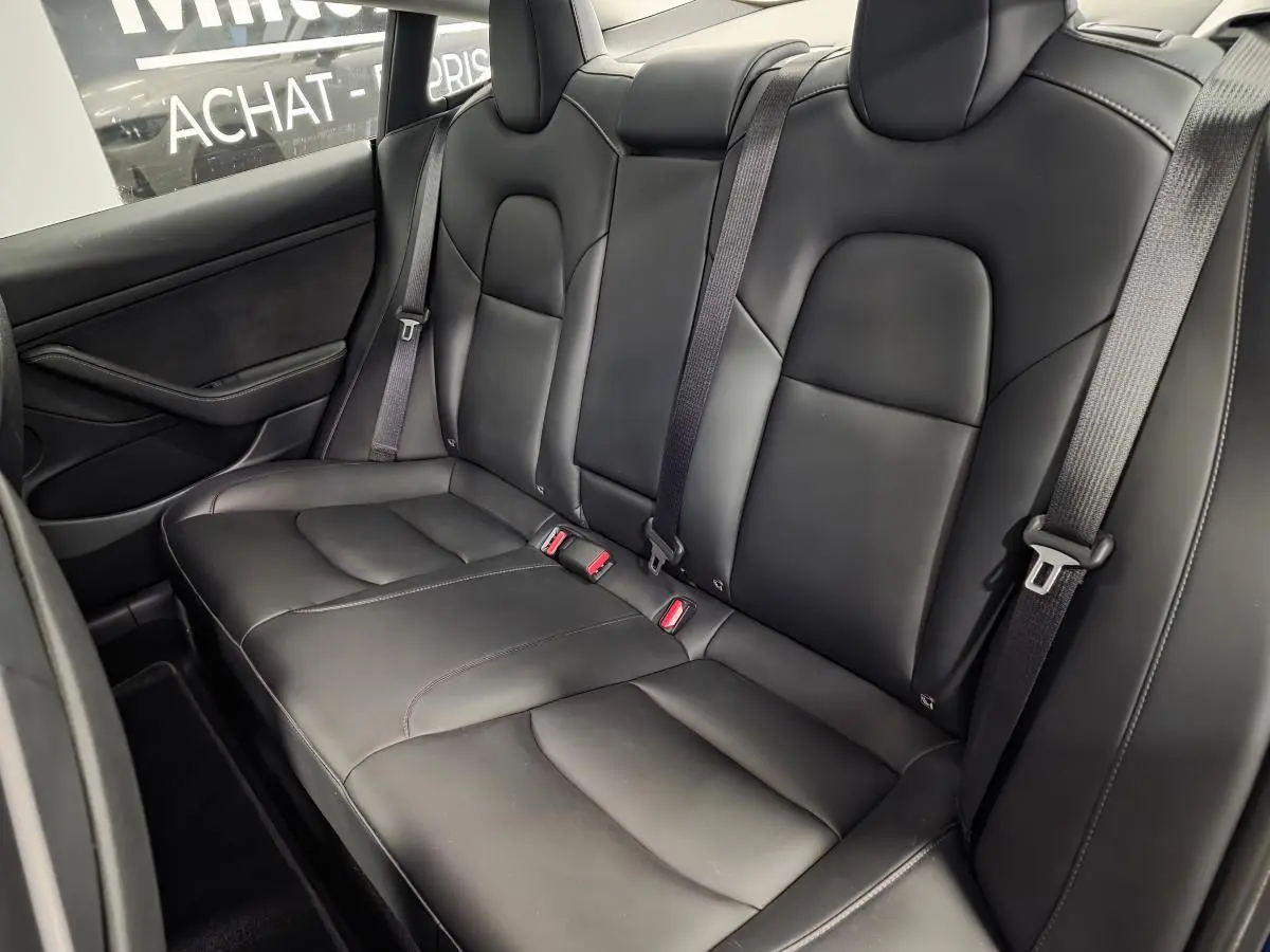 Vue latérale intérieure des sièges arrière noirs en cuir d'une Tesla Model 3 RWD 2021 avec ceintures grises.