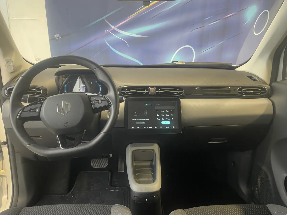 Vue intérieure frontale du tableau de bord et volant cuir noir du Leapmotor T03 Luxury blanc avec écran tactile central.