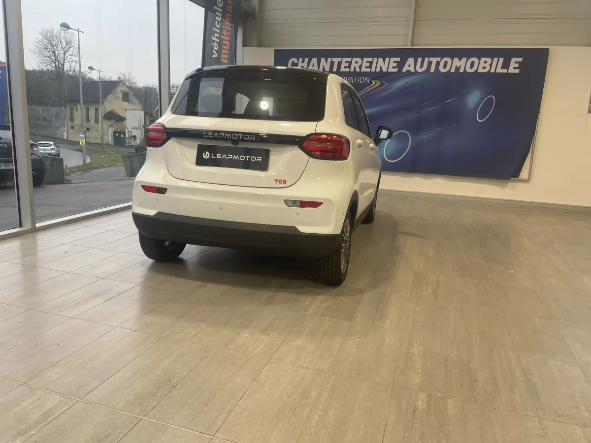Vue 3/4 arrière d'une Leapmotor T03 Luxury blanche en showroom, avec feux arrière LED et toit noir contrastant.