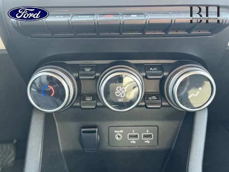 Vue rapprochée des commandes de climatisation et des ports USB sur la console centrale d'une Renault Clio gris Platine 2023.