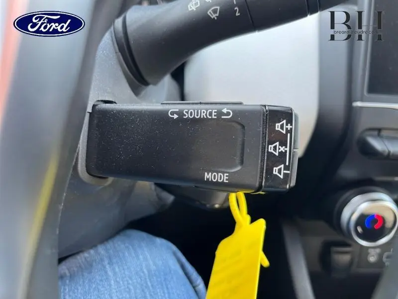 Gros plan sur la commande au volant noir avec boutons source et mode, intérieur d’une Renault Clio gris platine 2023.