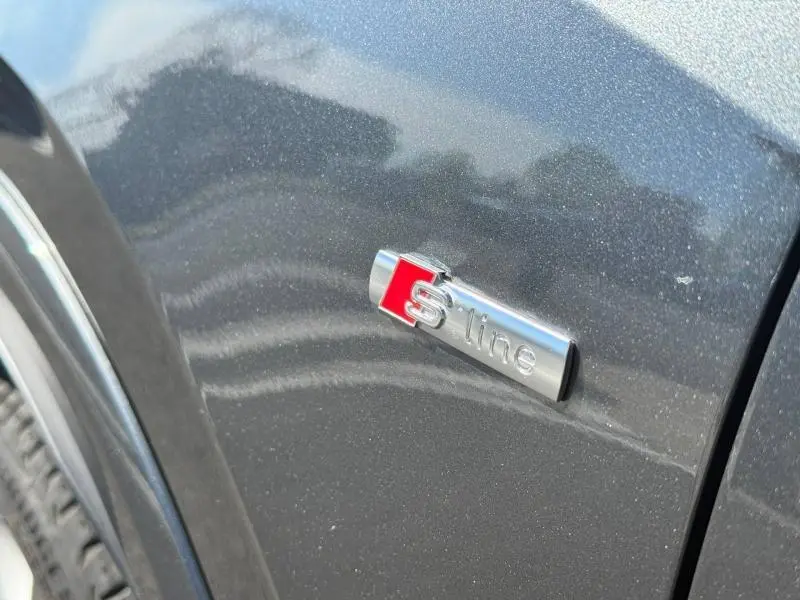 Gros plan sur l'emblème S line argent et rouge sur la carrosserie gris Daytona nacré d'un Audi Q2 2025.