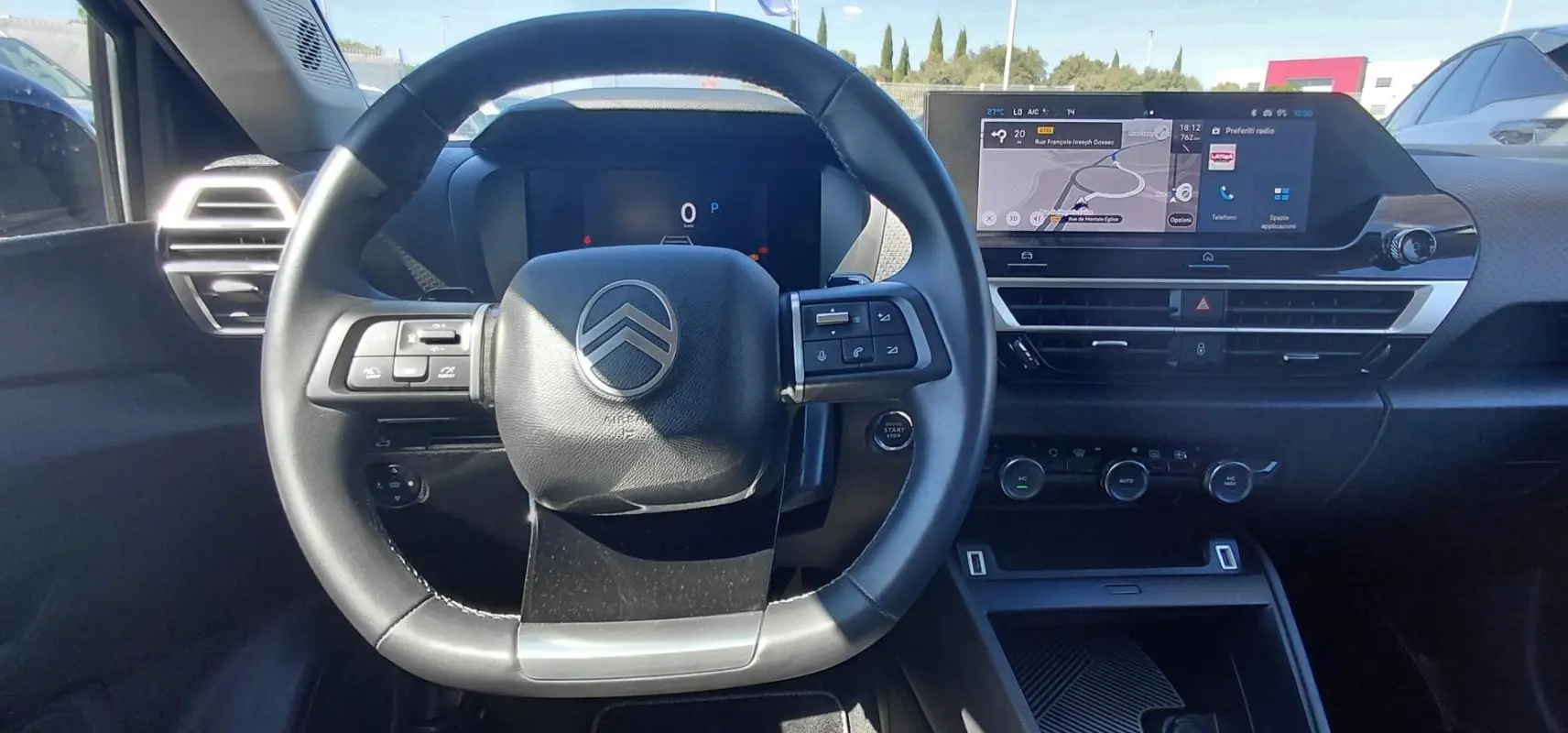 Vue intérieure centrée sur le volant cuir noir et le tableau de bord numérique du Citroën C4 X hybride 2025.