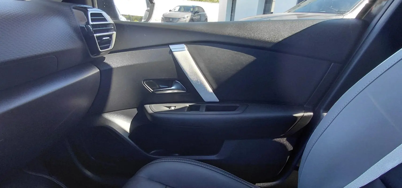 Vue intérieure côté passager avant de la Citroën C4 X 2025, montrant la porte noire et le siège en cuir gris.