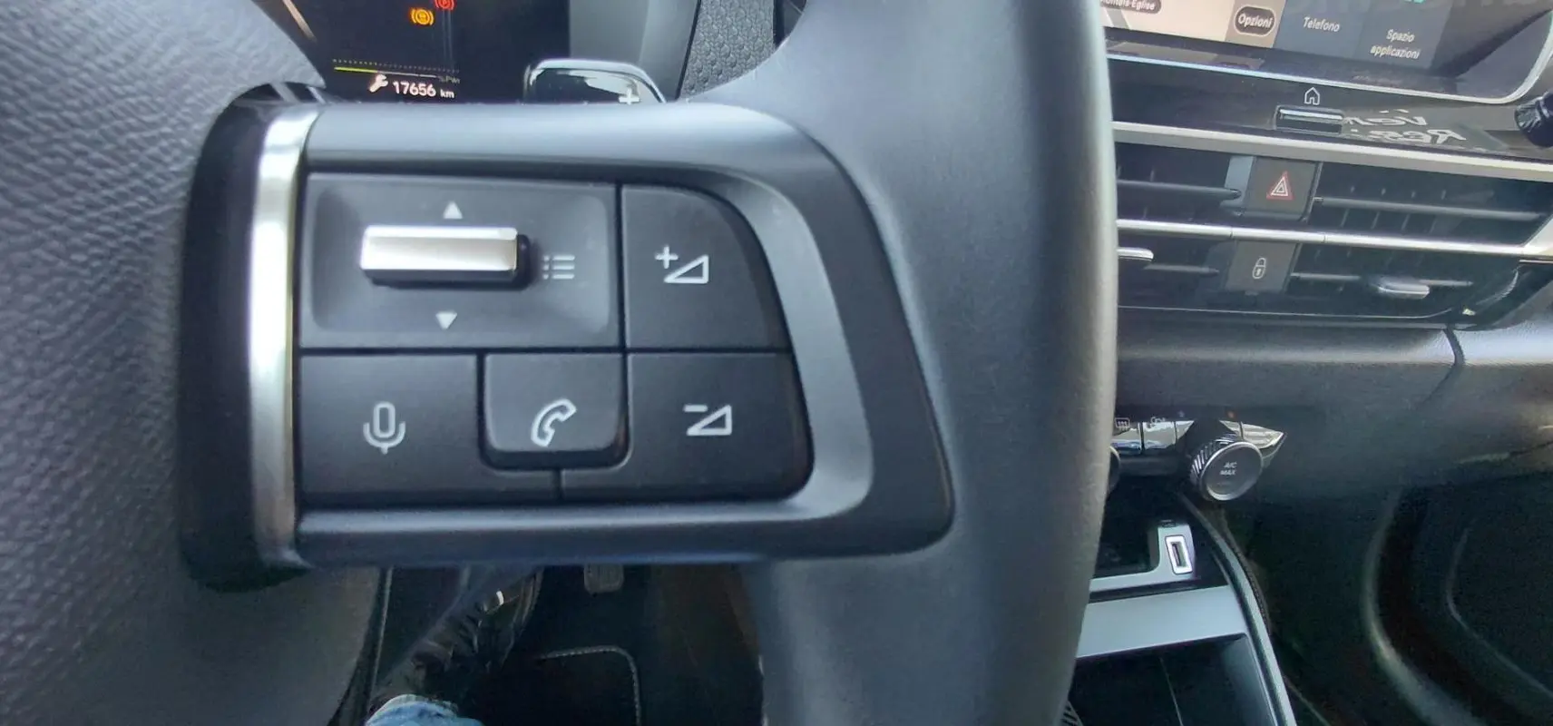 Gros plan sur les commandes du volant noir de la Citroën C4 X hybride 2025, avec tableau de bord et console en arrière-plan.