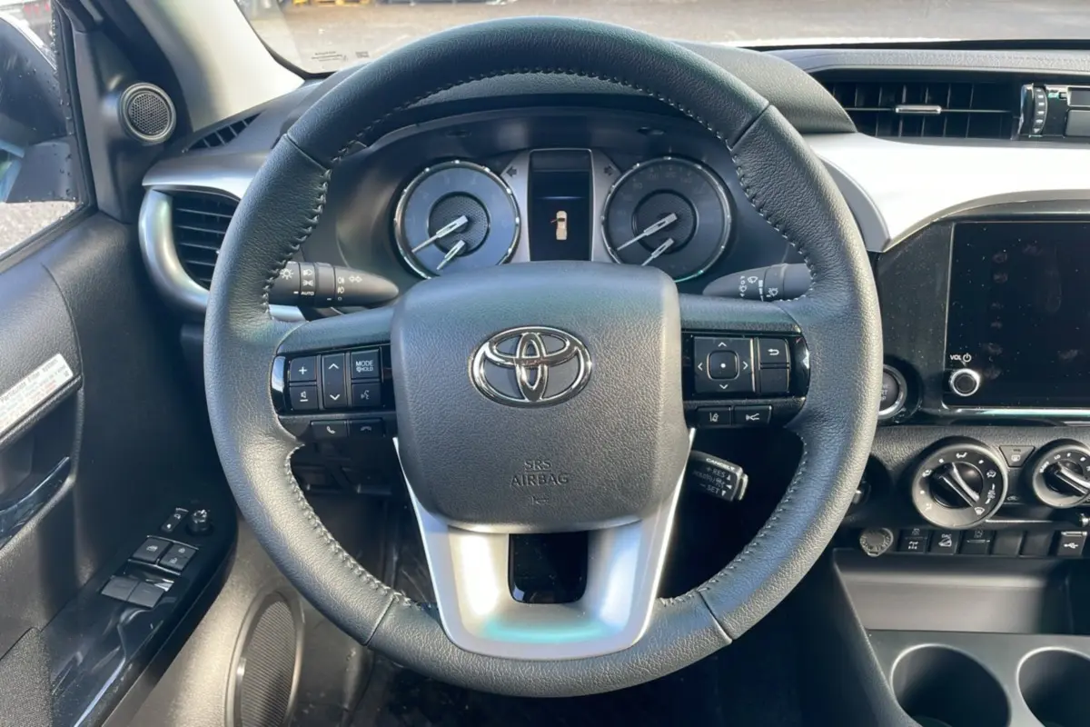 Vue intérieure centrée sur le volant cuir du Toyota Hilux 2025 avec tableau de bord et commandes visibles.