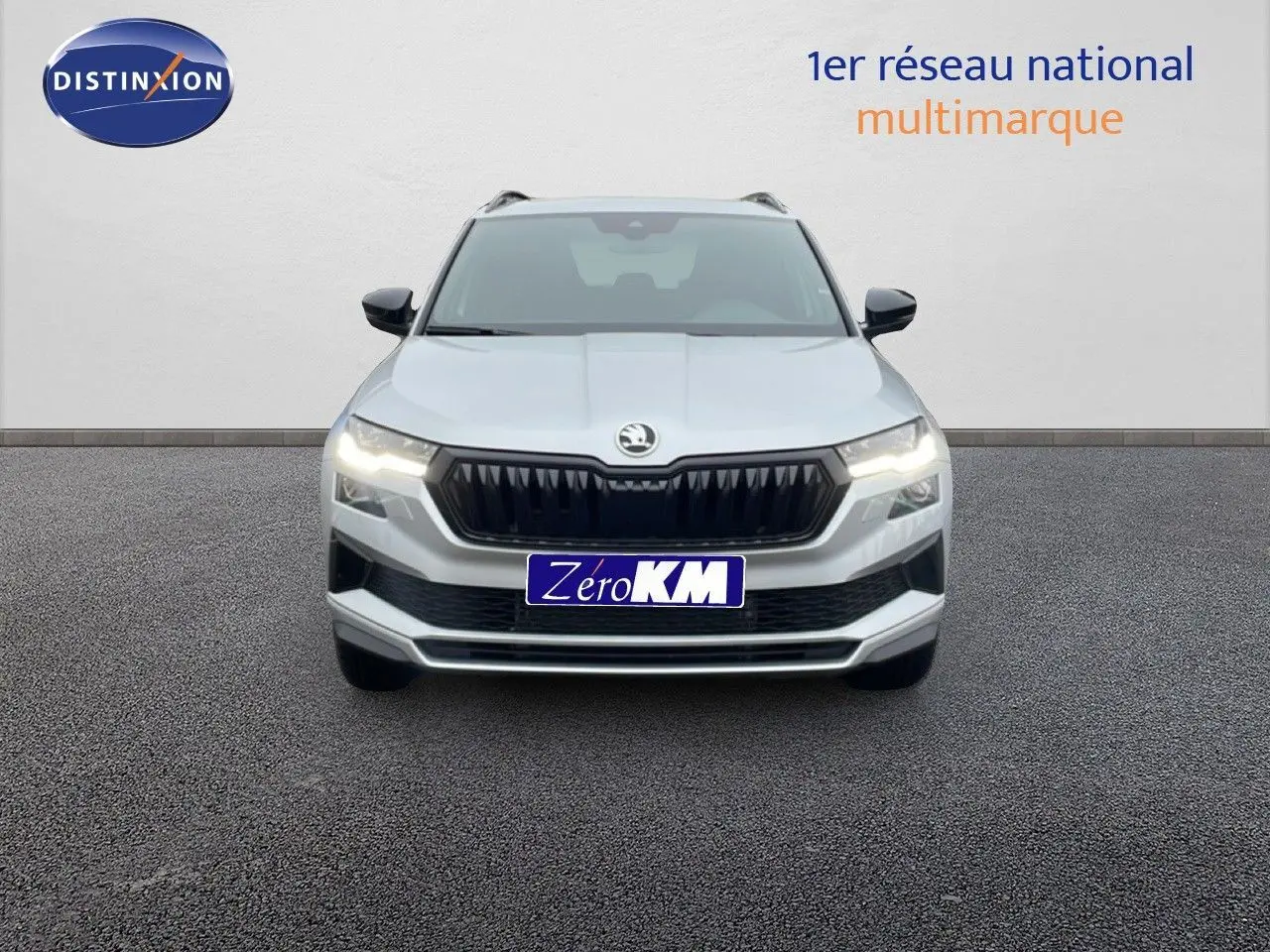 Vue frontale d’un Skoda Karoq gris argent métal 2025 avec calandre noire et feux LED allumés sur fond neutre.