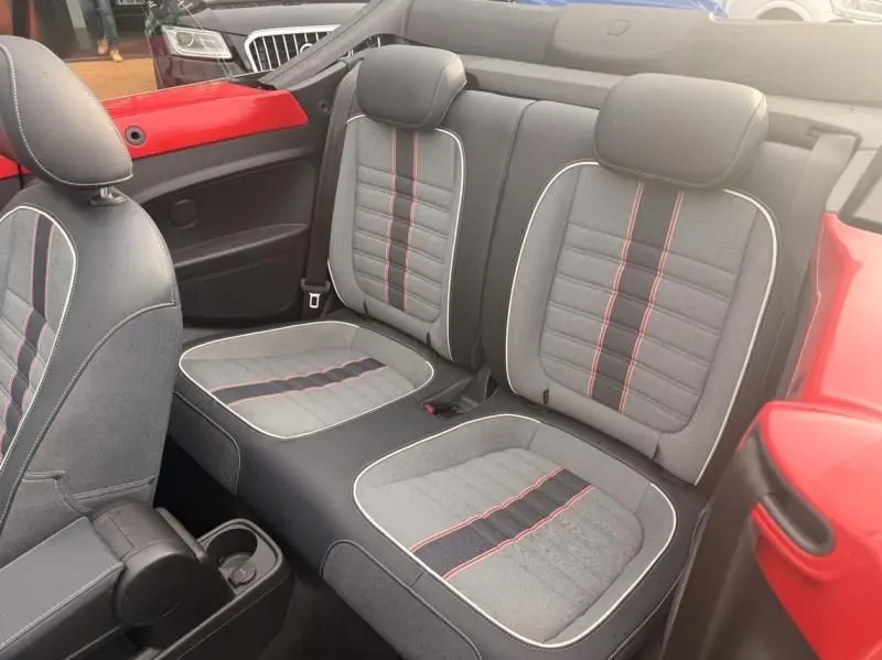 Vue intérieure arrière montrant les sièges en tissu gris avec surpiqûres rouges d'une Volkswagen Coccinelle Cabriolet rouge.