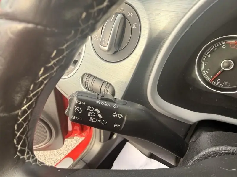 Gros plan sur la commande de clignotants et phares dans l'habitacle d'une Volkswagen Coccinelle Cabriolet rouge, vue côté conducteur.