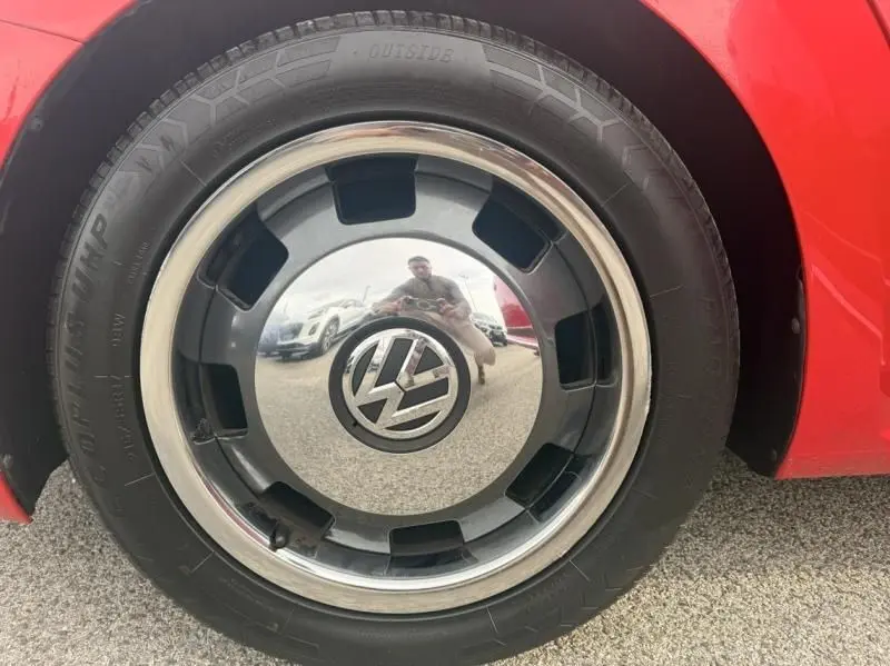 Gros plan sur la roue avant droite rouge d'une Volkswagen Coccinelle Cabriolet 2016 avec jante chromée et logo VW central.