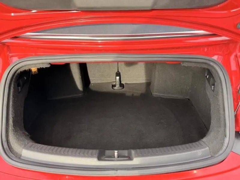 Vue intérieure du coffre ouvert d'une Volkswagen Coccinelle Cabriolet rouge 2016, montrant un espace de rangement vide.