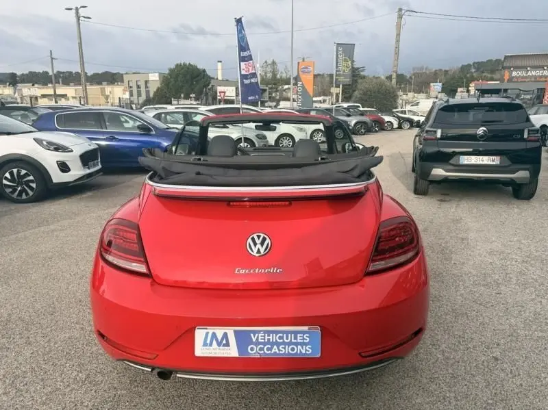 Vue arrière d'une Volkswagen Coccinelle Cabriolet rouge 2016 avec capote rabattue, en extérieur sur un parking.