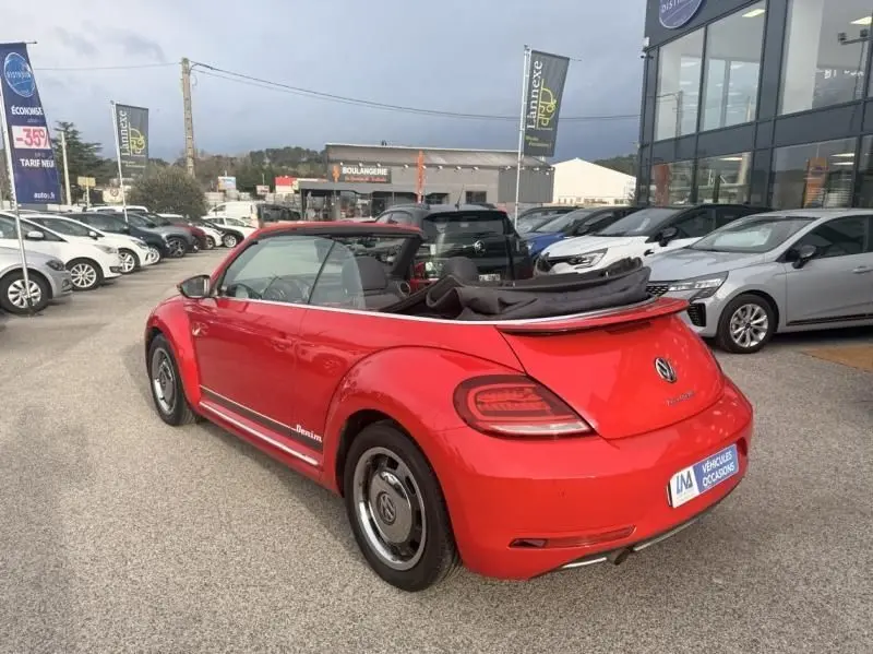 Vue 3/4 arrière droite d'une Volkswagen Coccinelle Cabriolet rouge 2016 avec capote ouverte et finition Denim visible sur le côté.