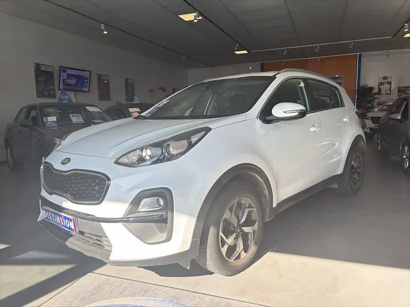 KIA SPORTAGE blanc vue 3/4 avant droit dans un showroom, avec jantes alliage et calandre noire distinctive.