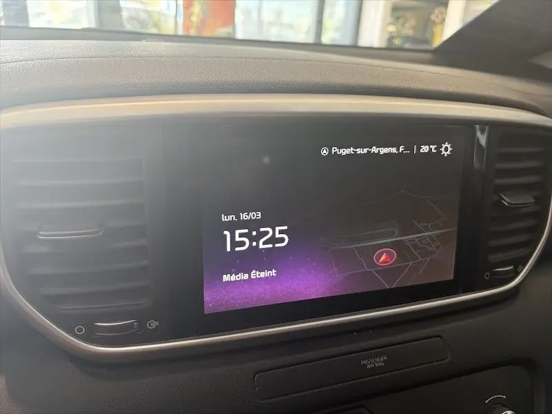 Vue rapprochée de l’écran tactile central du tableau de bord du Kia Sportage blanc, affichant l’heure et la navigation.