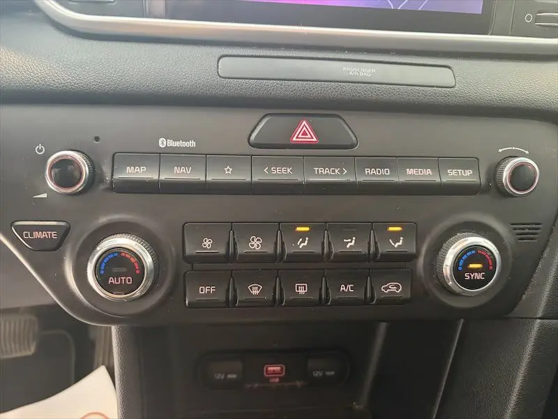 Tableau de bord du Kia Sportage blanc 2021, vue centrée sur les commandes de climatisation et multimédia avec boutons rétroéclairés.