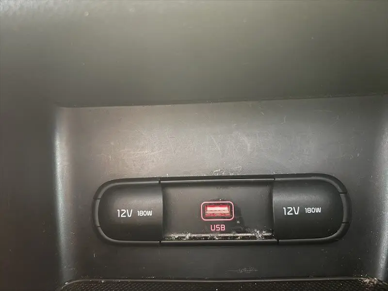 Gros plan sur la prise USB rouge encadrée de deux prises 12V noires dans l'habitacle du Kia Sportage blanc.
