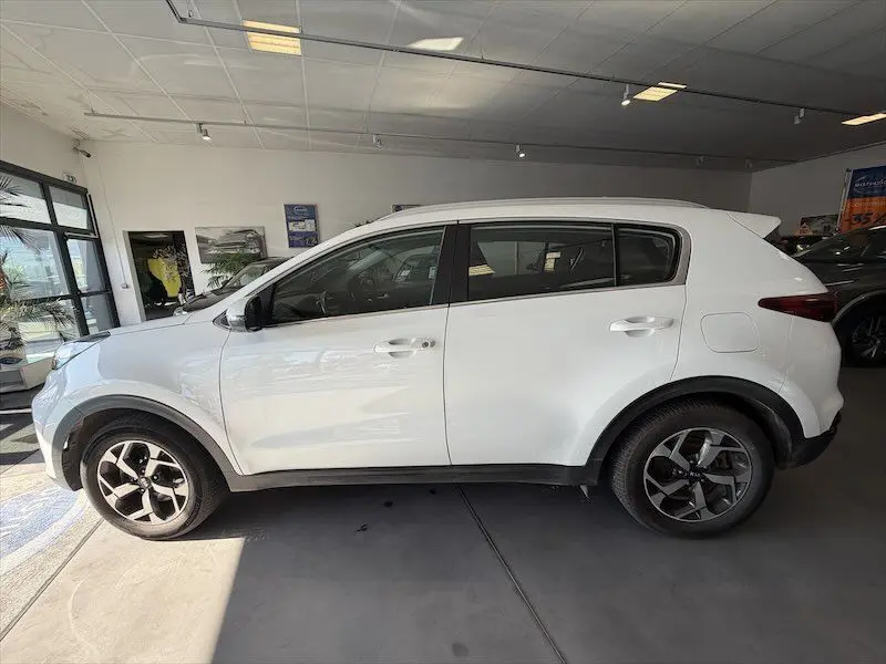 Vue de profil côté gauche d'un KIA Sportage blanc 2021 en intérieur, avec jantes bi-ton et vitres teintées.