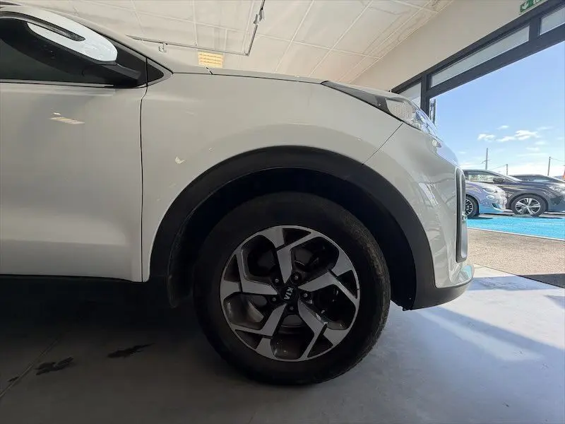 Gros plan sur la roue avant droite d’un KIA Sportage blanc 2021, mettant en valeur la jante bi-ton et le passage de roue noir.