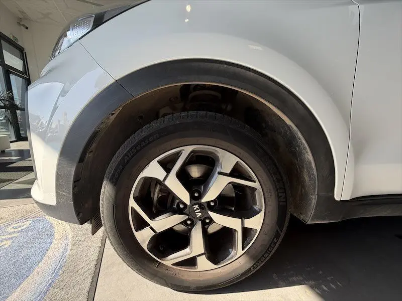 Gros plan sur la roue avant gauche d’un KIA Sportage blanc 2021, mettant en valeur la jante alliage bicolore.