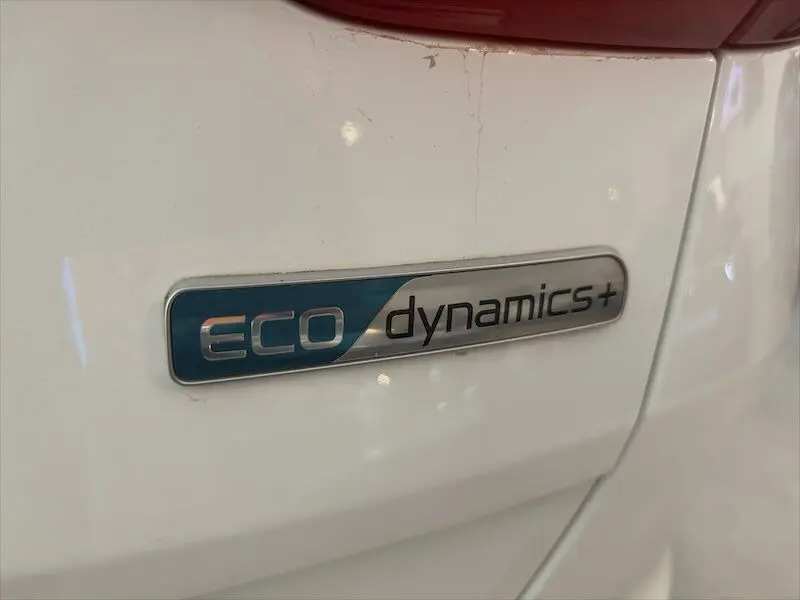 Gros plan sur l'écusson Eco Dynamics+ argent et bleu sur la carrosserie blanche arrière d'un Kia Sportage 2021.