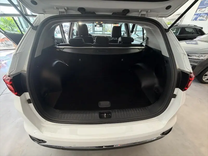 Vue arrière ouverte du coffre spacieux d'un Kia Sportage blanc 2021, avec banquette arrière et cache-bagages visibles.