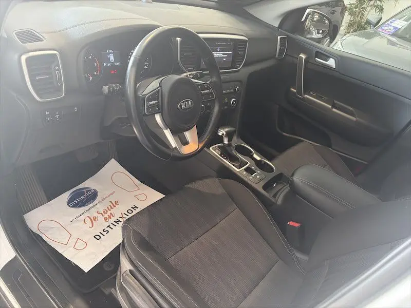 Vue intérieure côté conducteur du Kia Sportage blanc 2021, avec tableau de bord moderne et volant multifonction.