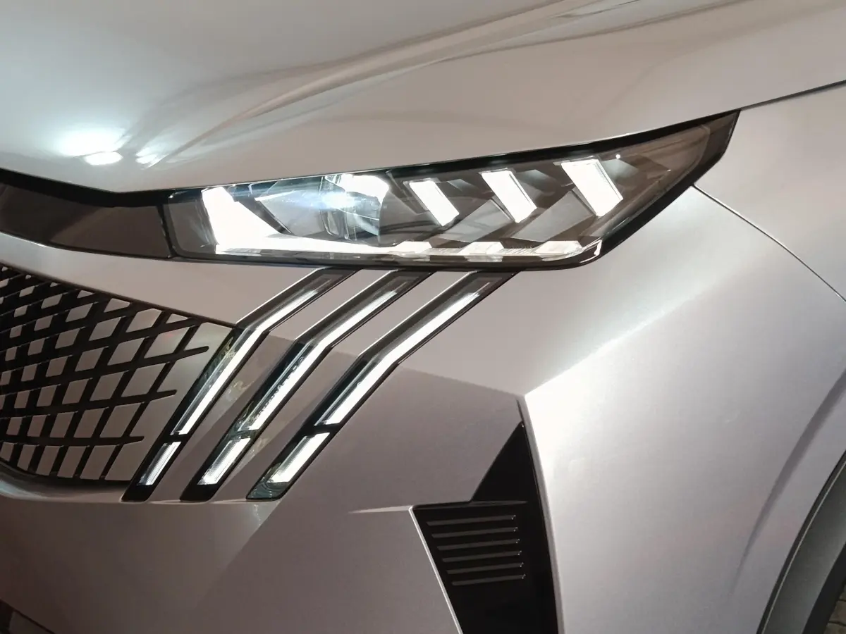 Gros plan sur l'avant droit gris clair du Peugeot 5008 2026, mettant en valeur ses phares LED et sa calandre distinctive.