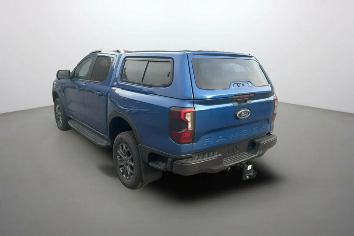 Ford Ranger 3.0 V6 Wildtrak bleu lightning, vue 3/4 arrière droit avec hard-top vitré et attelage.